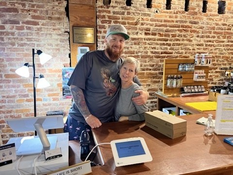Two small business owners smiling behind the counter next to their POS system